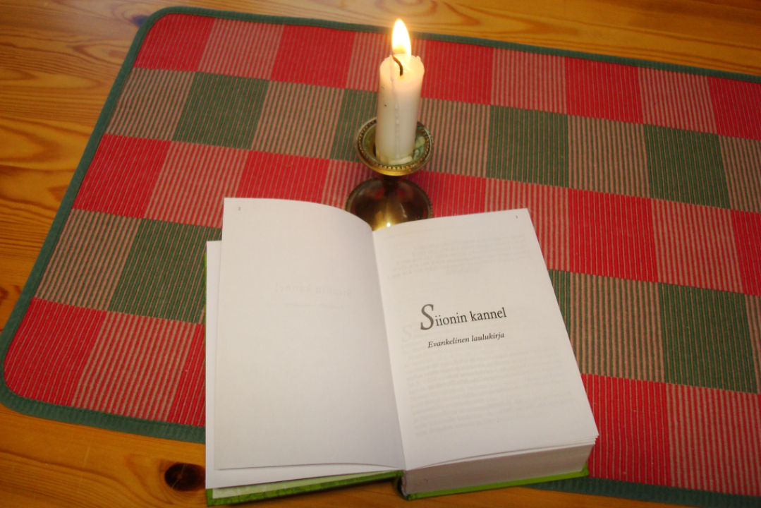 Siionin kannel laulukirja avattuna pöydällä ja kynttilä palaa vieressä.