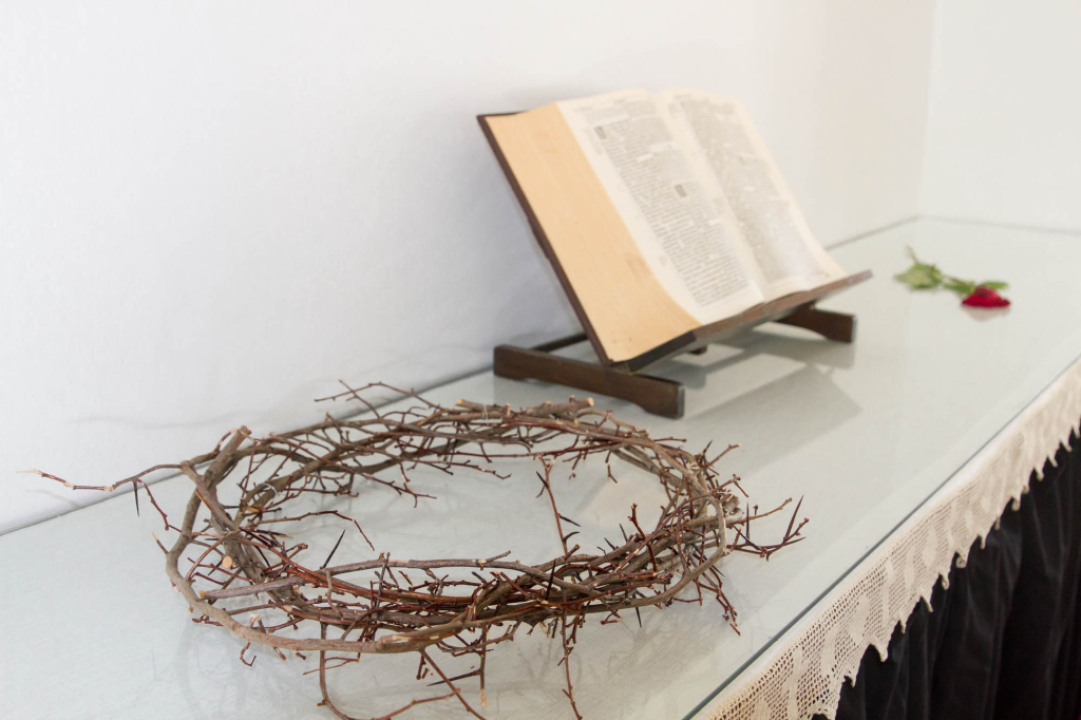 Kuvassa orjantappurakruunu, raamattu ja yksi ruusu alttarin päällä lappeellaan.