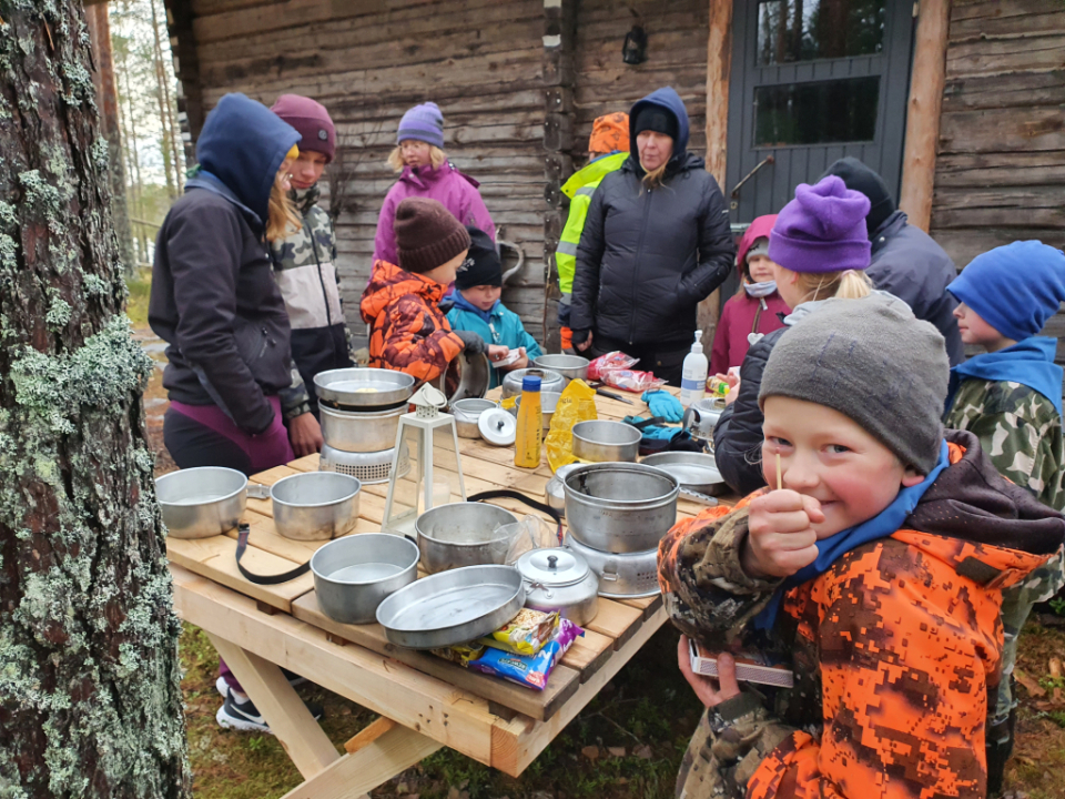 Lapset ovat ulkona pöydän ympärillä. Pöydällä on retkikeittimiä.