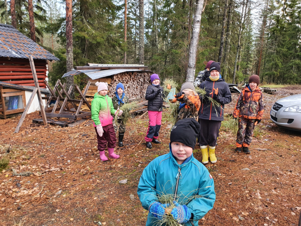 Lapset seisovat ulkona heinätukot ja porkkanat käsissään.