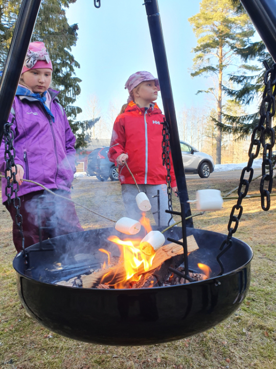 Lapset paistavat vaahtokarkkeja tikunnokassa nuotiolla.