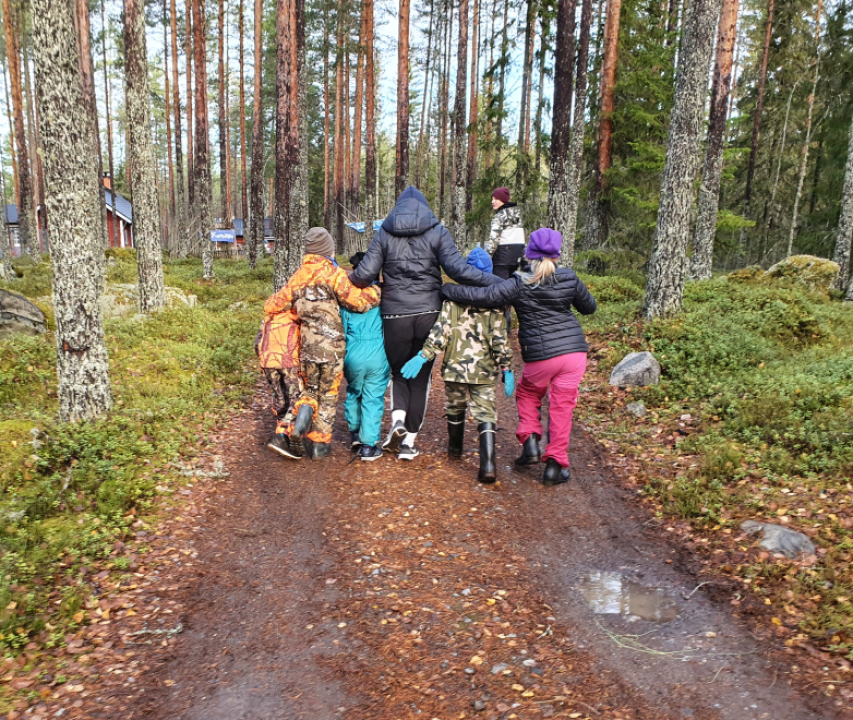 Lapset kävelevät tietä pitkin kädet toistensa olkapäillä.